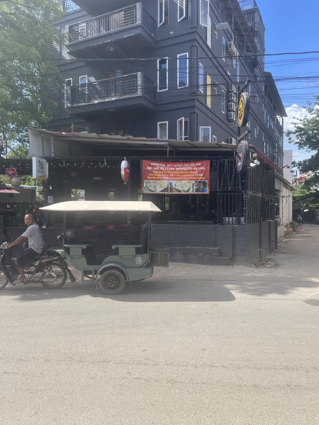 Motorcyclists on a busy Cambodian street with storefronts and Khmer signage