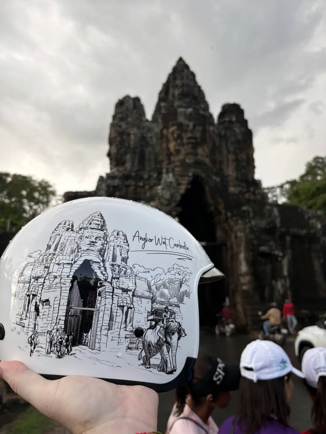 Jim holding a white helmet with Angkor temple artwork in front of Bayon Temple