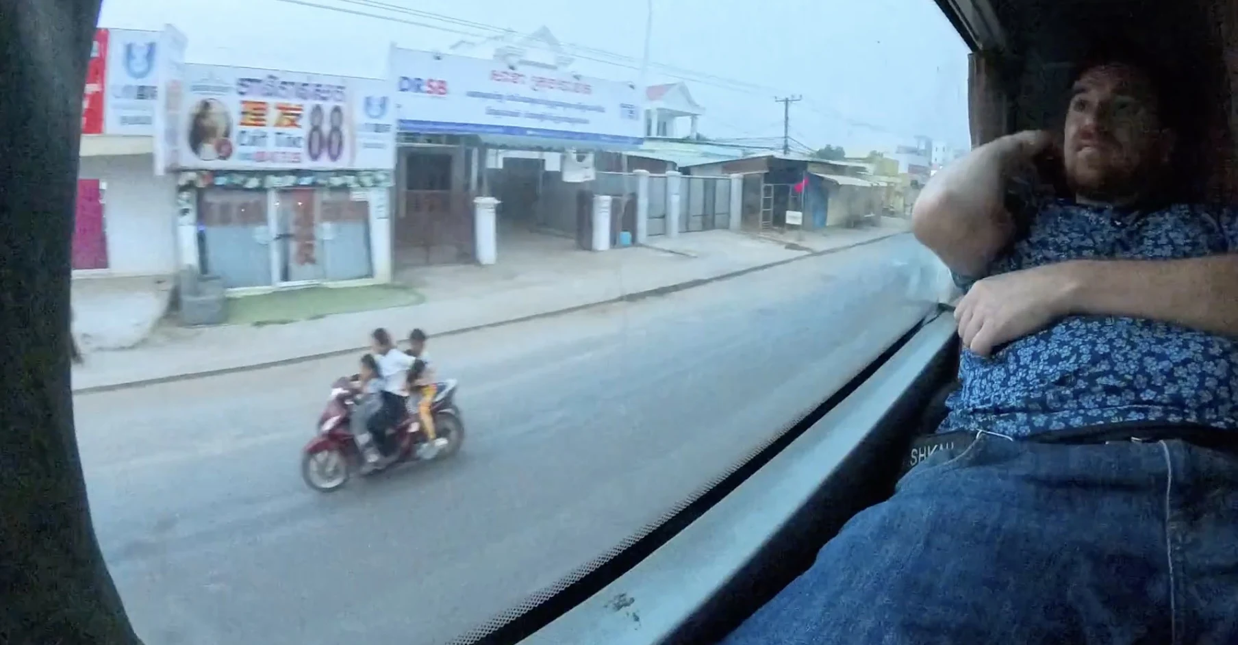 Jim watching three children ride a scooter without helmets through a bus window in Cambodia