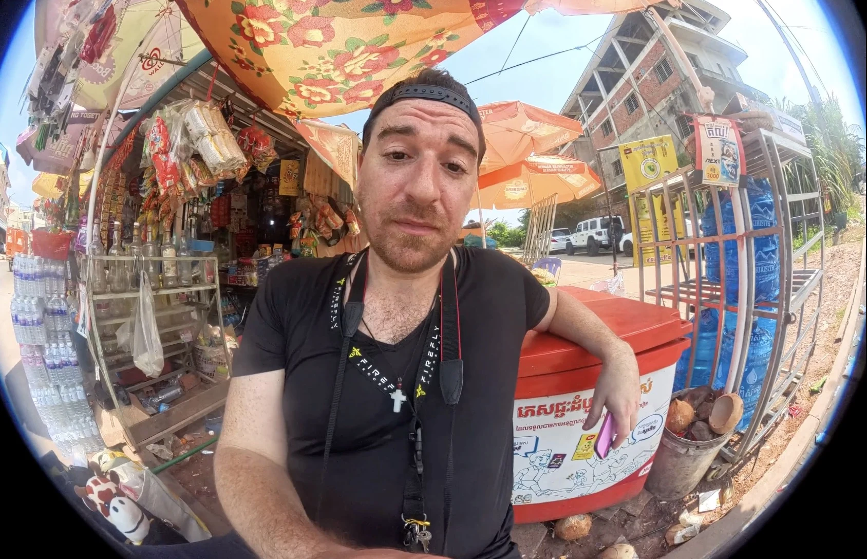 Jim at a Cambodian roadside market, fisheye selfie showing the street vendor scene