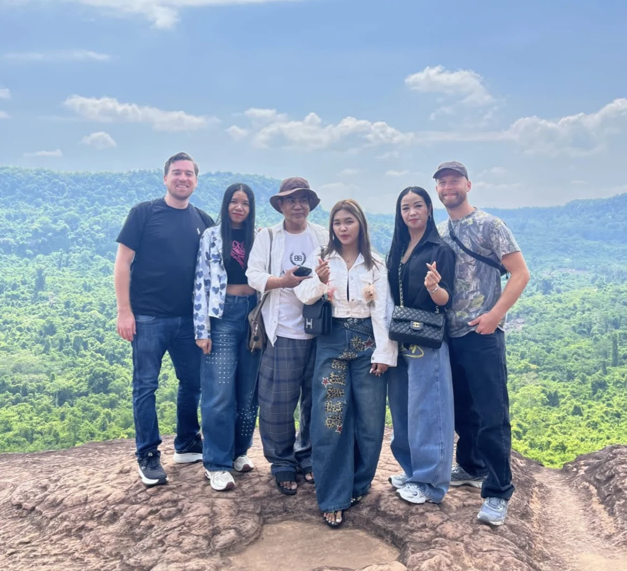 Jim and five others posing together on a rocky hilltop overlook above a lush forested Cambodian valley