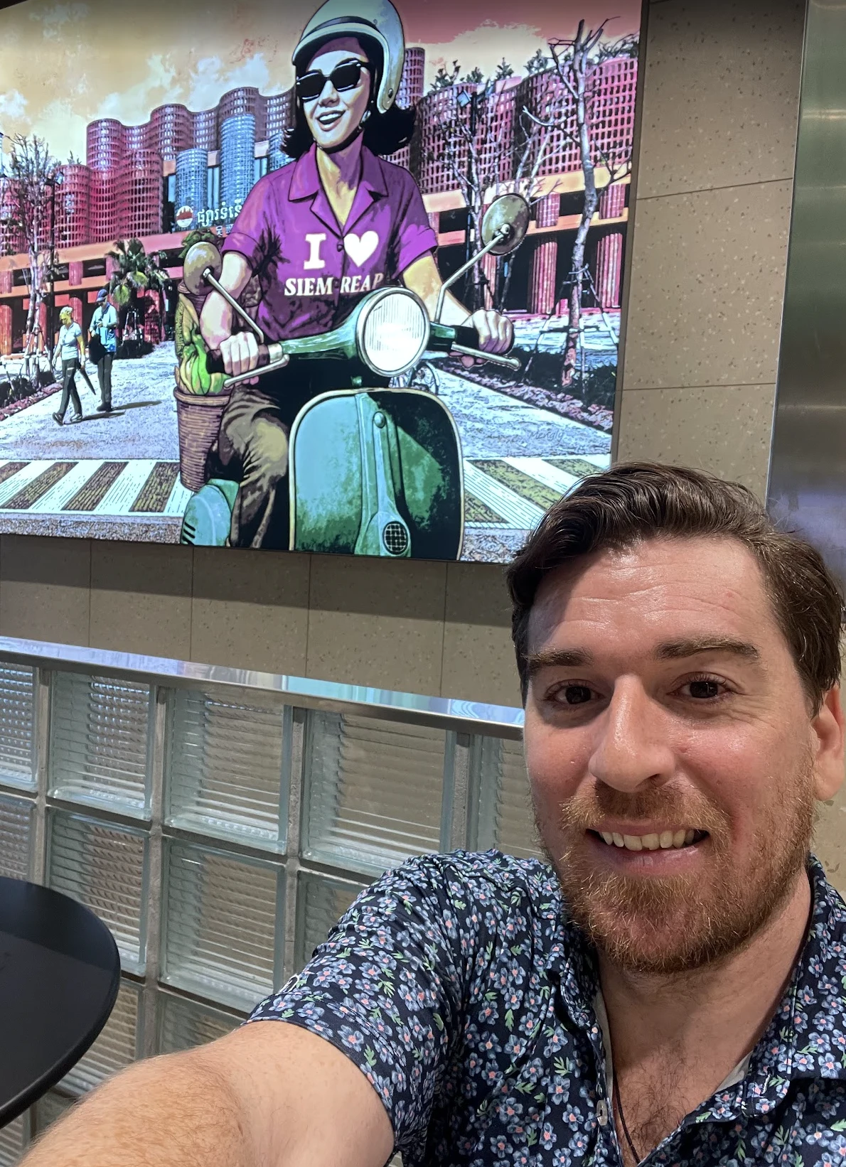 Jim taking a selfie in front of a colorful mural at Siem Reap airport