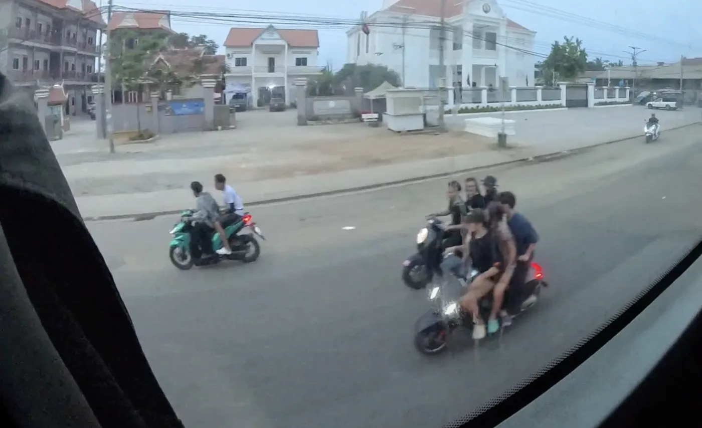 Multiple motorcycles with children showing varied helmet use on a Cambodian road