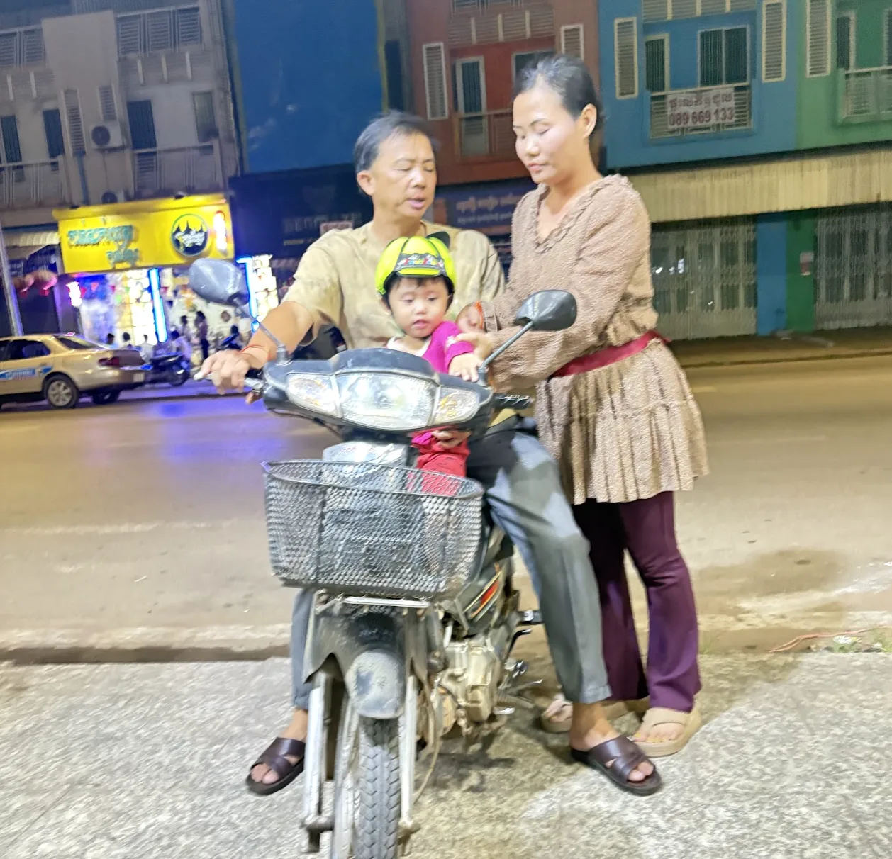 Family of three on a motorcycle at night, young child wearing a bright yellow helmet